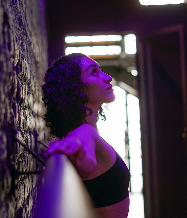 Woman in a flowing yoga pose in a dark studio with purple light.